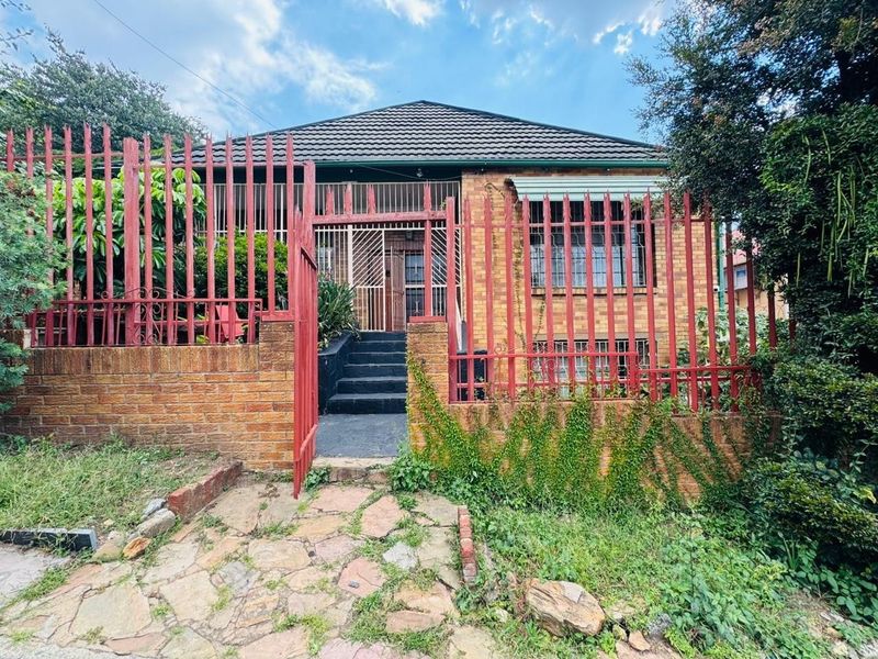 Front elevation of a brick house featuring a tiled roof, secure perimeter fencing, and a gated entrance with concrete steps.