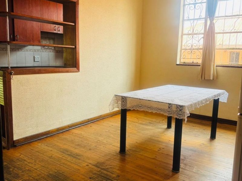 Dining area featuring original hardwood flooring, built-in wall cabinetry, and a window with security bars, offering a blank canvas for renovation.