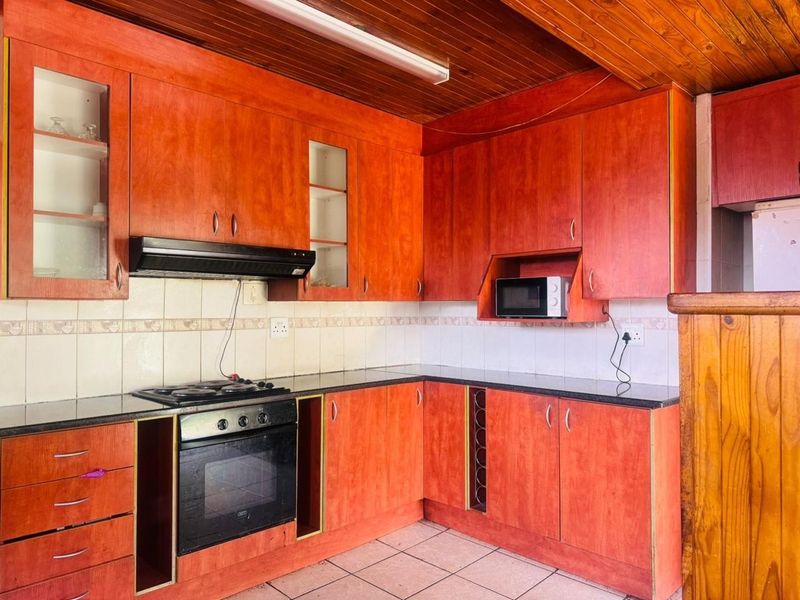 A functional kitchen featuring wooden cabinetry, granite countertops, built-in oven, hob, extractor fan, and a timber-clad ceiling.