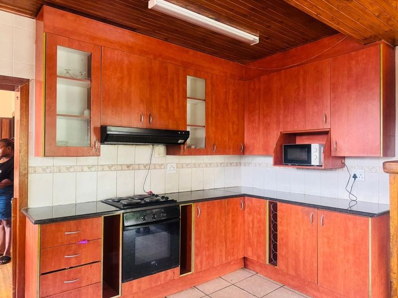 A functional kitchen featuring warm-toned wooden cabinetry, granite countertops, a built-in oven, and a distinctive timber-paneled ceiling.