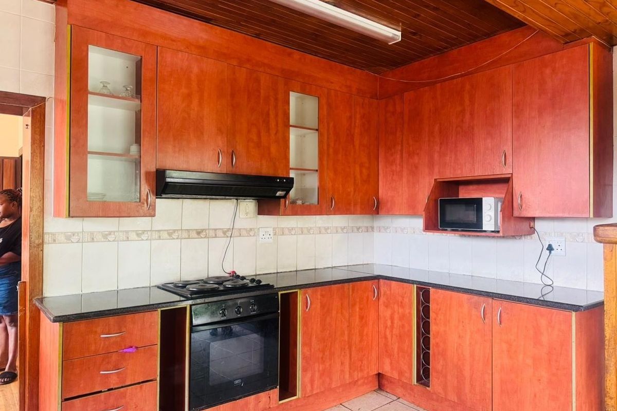 A functional kitchen featuring warm-toned wooden cabinetry, granite countertops, a built-in oven, and a distinctive timber-paneled ceiling.