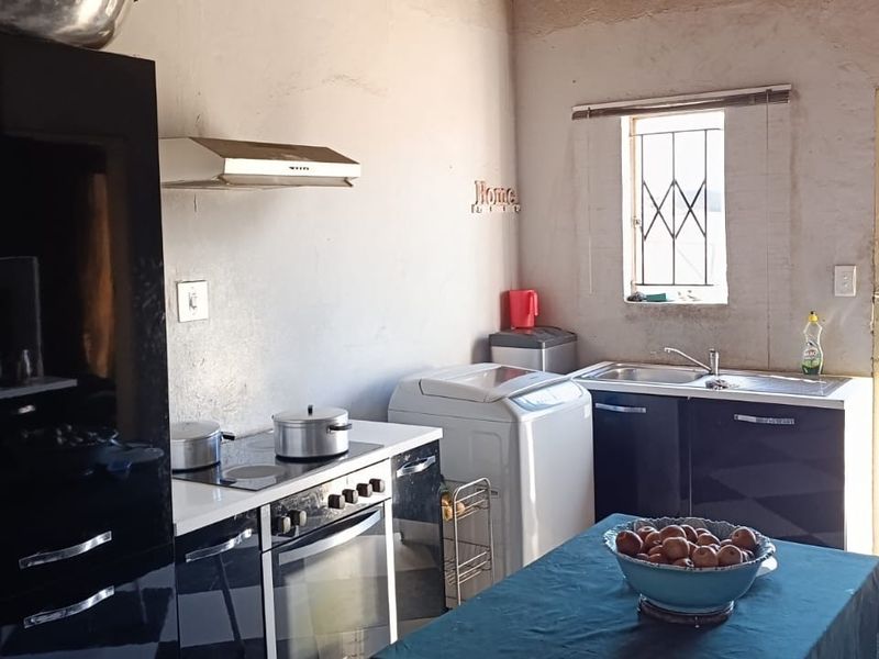 A functional kitchen featuring dark cabinetry, built-in oven and hob, extractor fan, and direct access to the rear exterior.