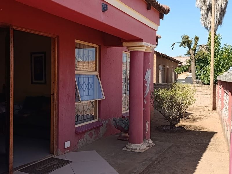 Front entrance area featuring a covered porch with decorative columns, security window bars, and a tiled threshold, showing signs of exterior wear.