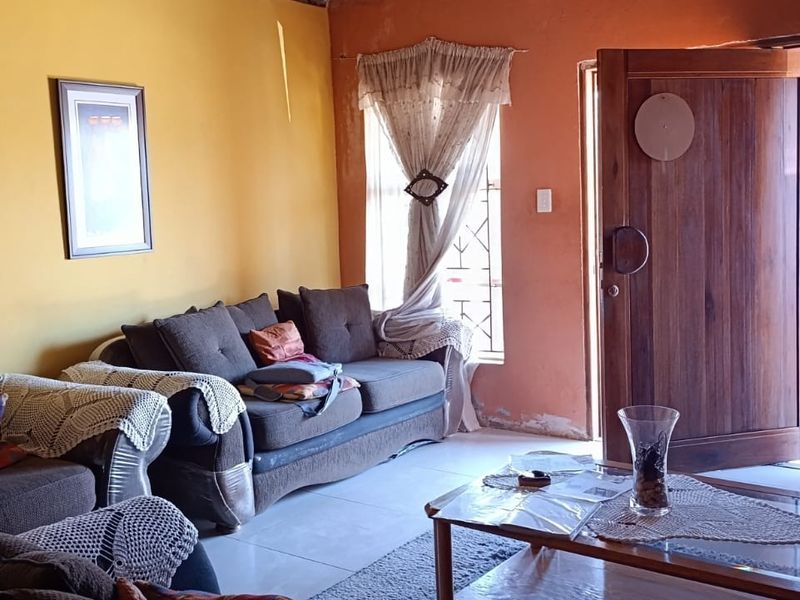 A living room featuring tiled floors, a solid timber entrance door, and windows fitted with security bars.