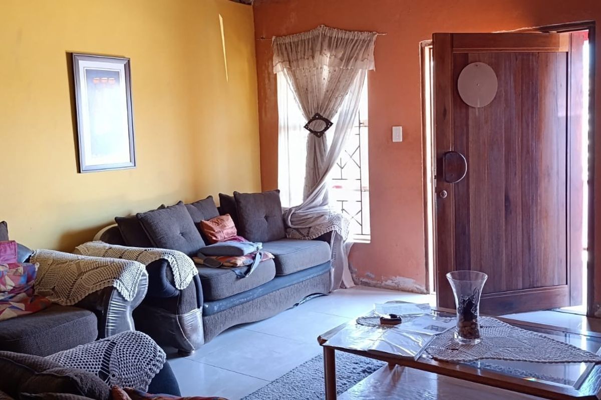 A living room featuring tiled floors, a solid timber entrance door, and windows fitted with security bars.