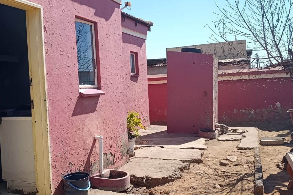 Rear exterior view of the property featuring a pink rendered facade, concrete paving, and a small yard area with a water tank.