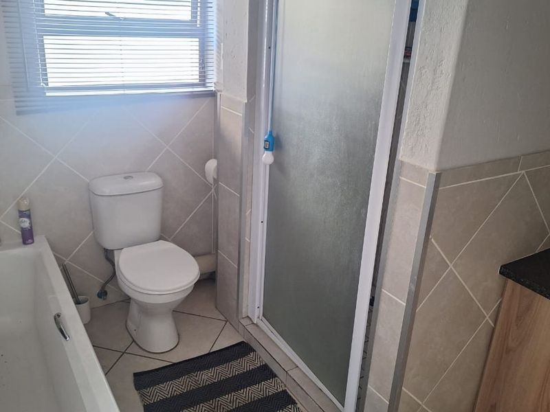 A functional bathroom featuring a bathtub, separate shower enclosure, toilet, and vanity cabinet with tiled finishes throughout.