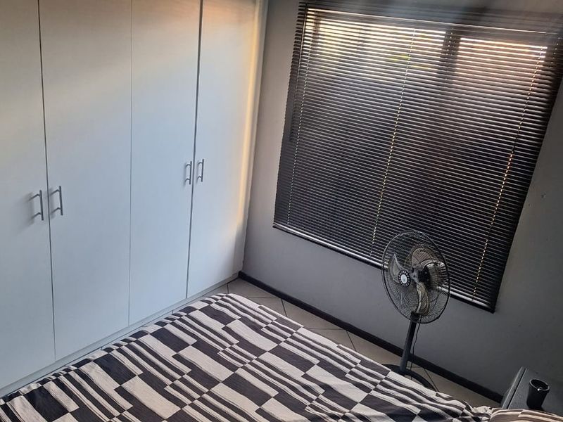 A bedroom featuring built-in cupboards, tiled flooring, and venetian blinds, providing a functional and neutral living space.