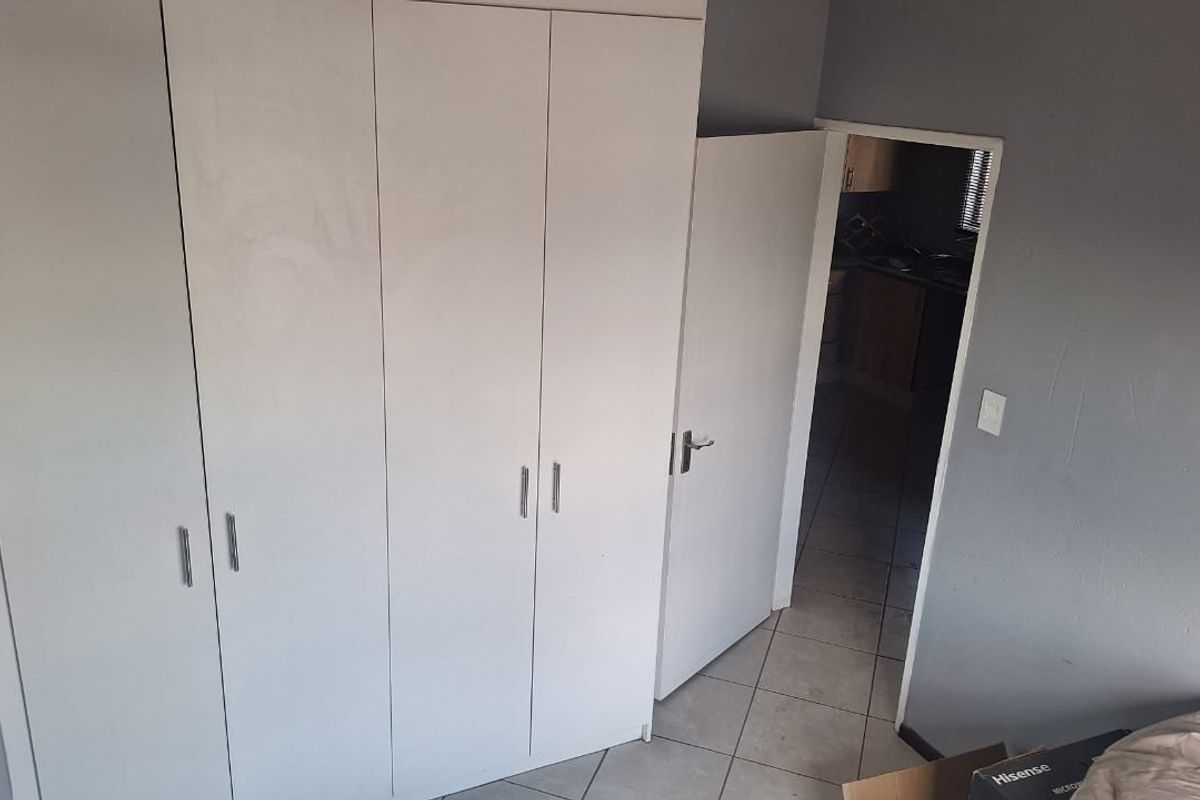 A bedroom featuring built-in cupboards and tiled flooring, with a doorway leading to an adjacent room.