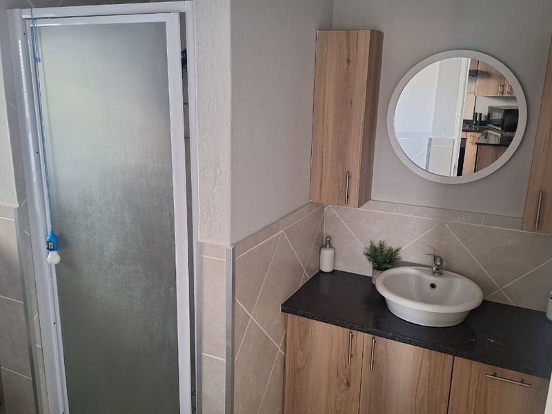 A well-maintained bathroom featuring a shower enclosure, a modern vanity with a vessel sink, and ample wall-mounted storage cabinetry.
