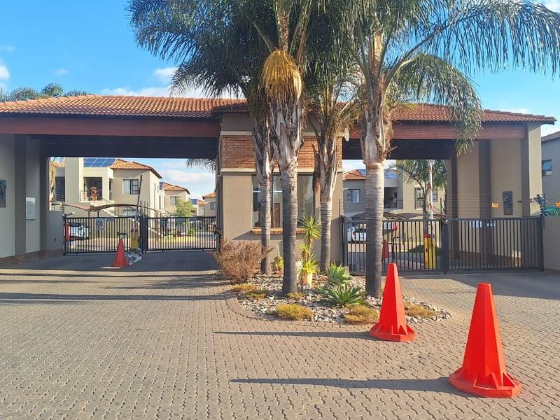 The main entrance to the apartment complex featuring a secure gated access point, guard house, and paved driveway.