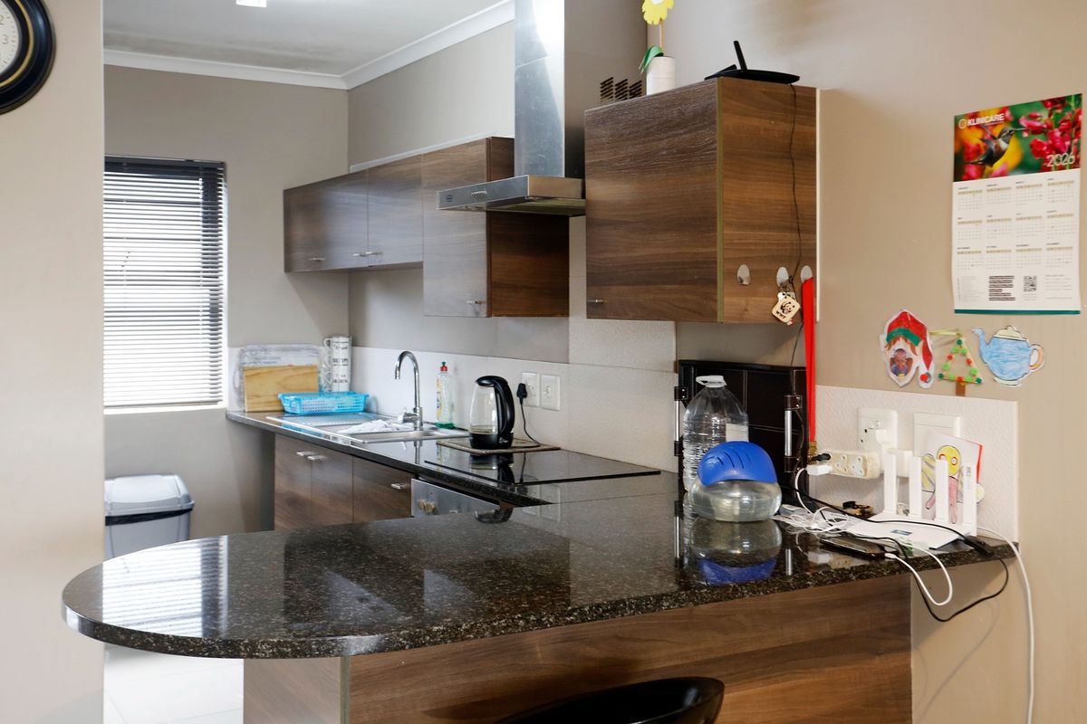 A functional kitchen featuring dark granite countertops, wood-finish cabinetry, a stainless steel extractor fan, and an electric hob with a breakfast bar extension.