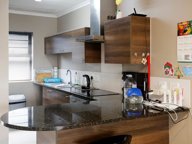 A functional kitchen featuring dark granite countertops, wood-finish cabinetry, a stainless steel extractor fan, and an electric hob with a breakfast bar extension.
