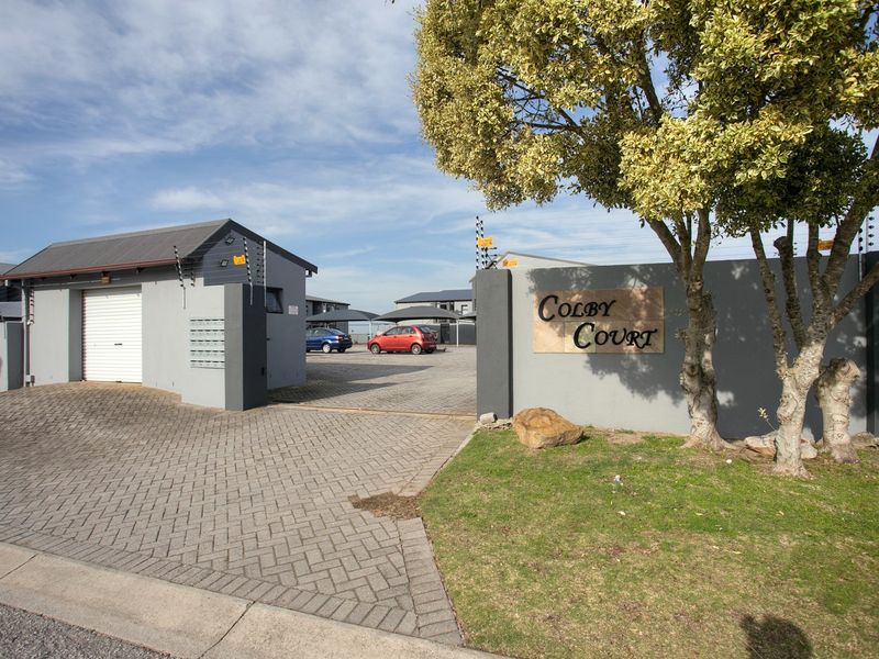 Front entrance view of Colby Court apartment complex featuring a paved driveway, secure boundary wall with electric fencing, and garage access.