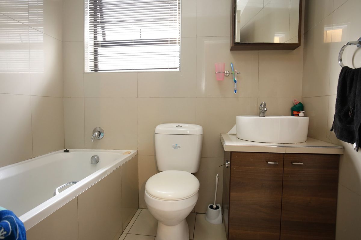 A functional bathroom featuring a bathtub, a modern vessel sink with vanity storage, a wall-mounted mirror cabinet, and neutral wall tiling.