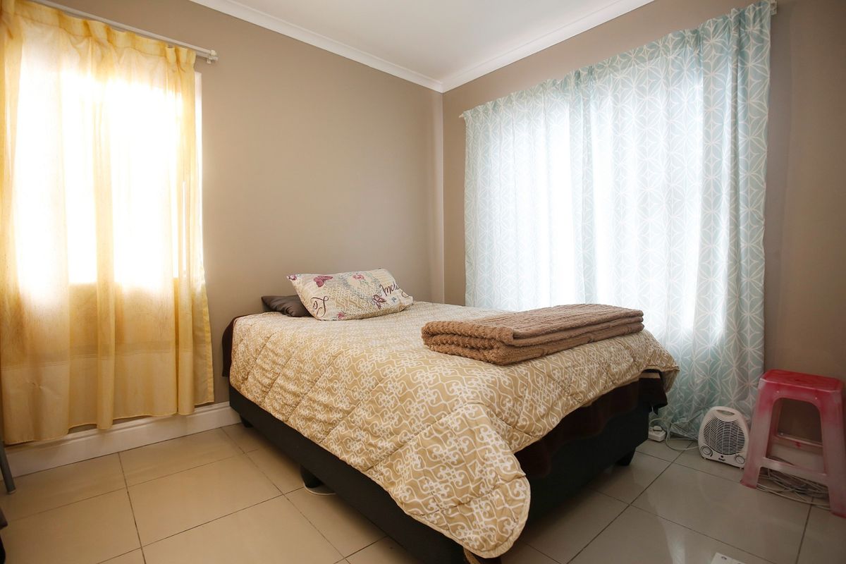 A bedroom featuring neutral wall paint, tiled flooring, and dual windows with curtain treatments.