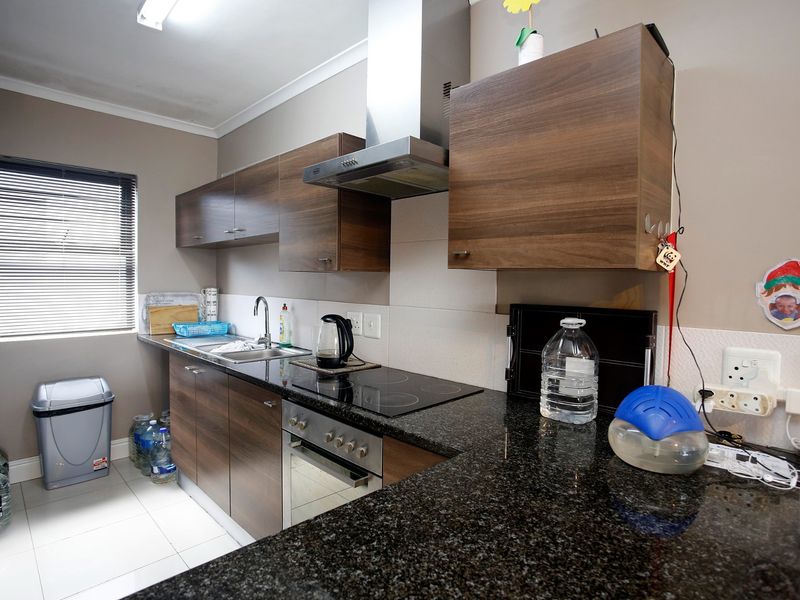 Modern kitchen featuring dark wood cabinetry, granite countertops, built-in oven, electric hob, and stainless steel extractor fan with tiled flooring.