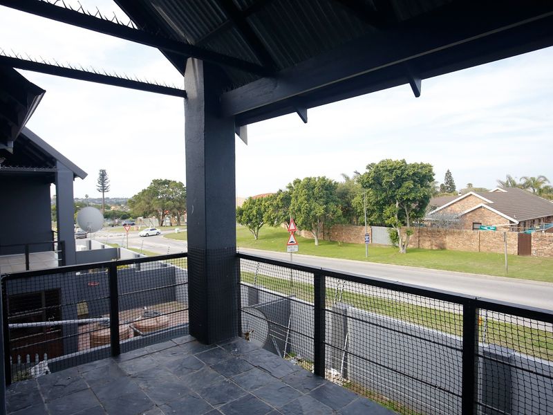 A covered balcony featuring dark tiled flooring, a sturdy metal railing, and a high-pitched roof structure overlooking the street.