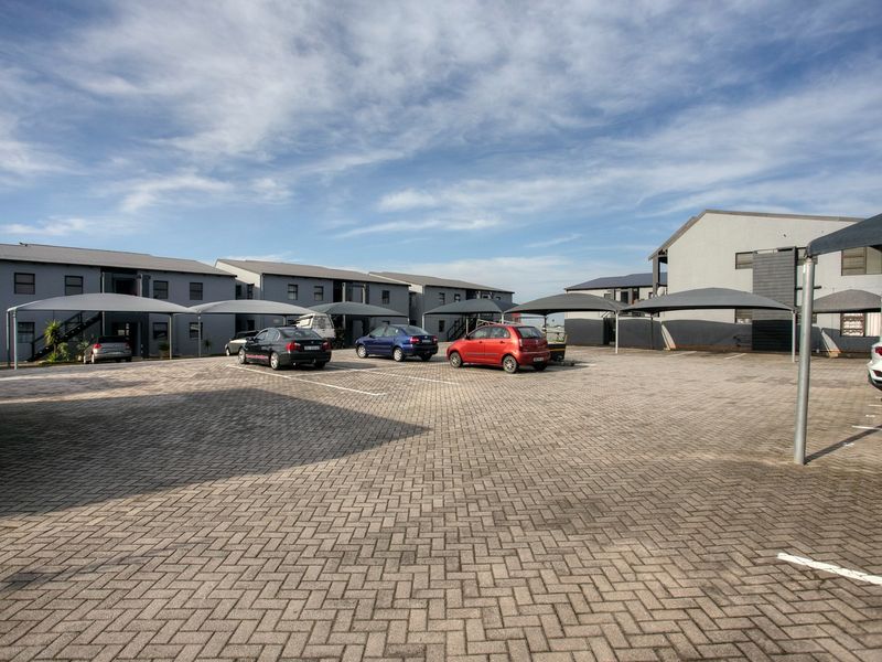 A view of the apartment complex exterior featuring a paved parking area with covered carports and multi-story residential building blocks.