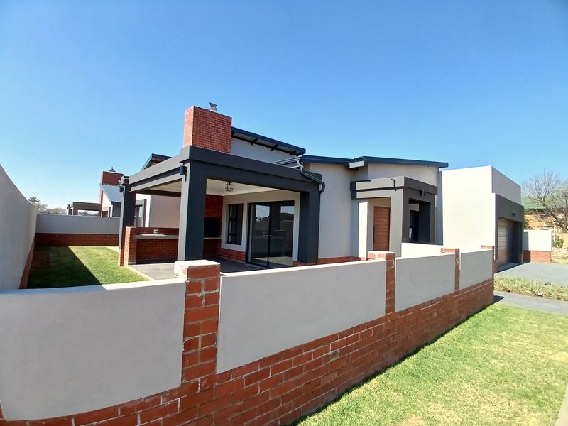 Rear view of a modern house featuring a covered patio with a built-in braai, brick chimney, and a private garden area.