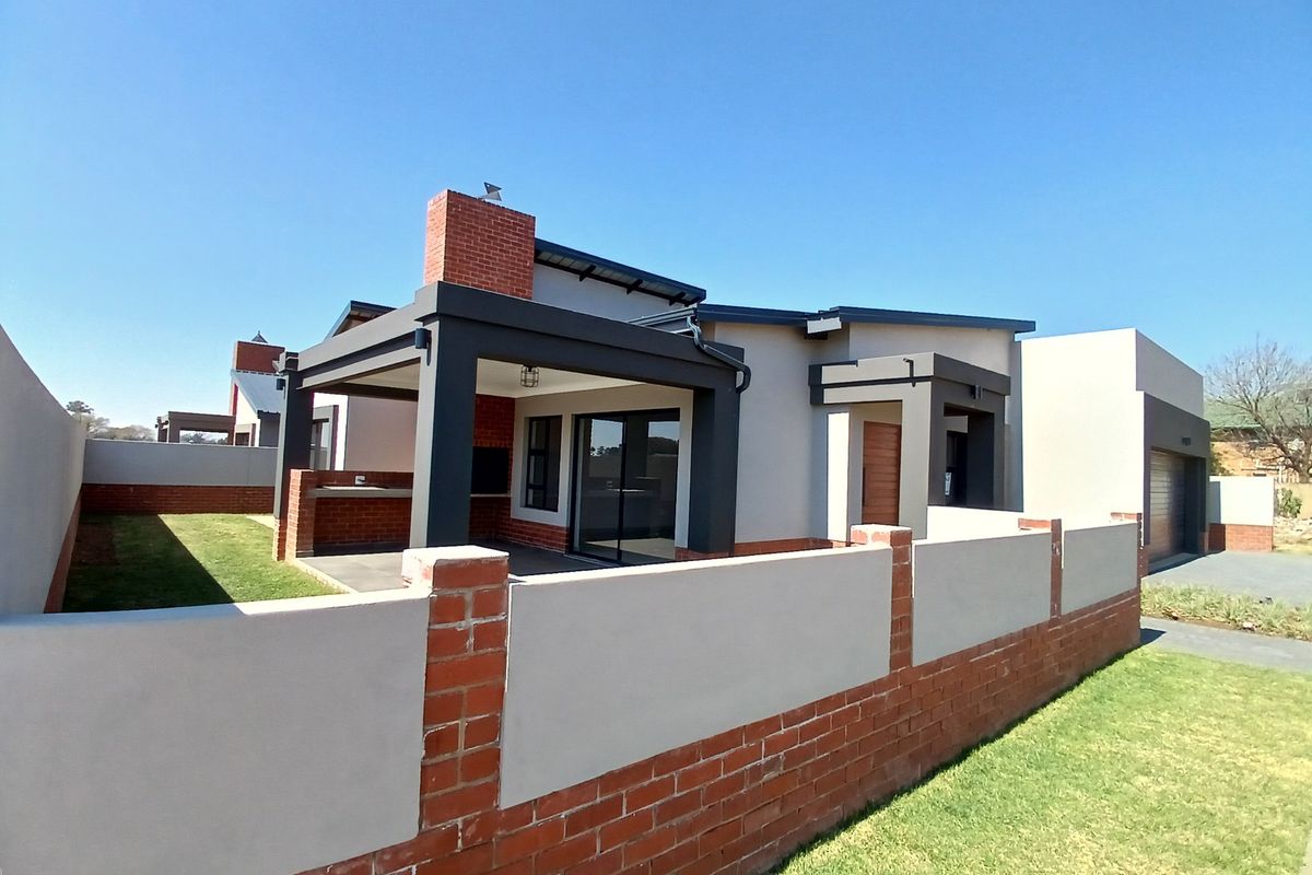 Rear view of a modern house featuring a covered patio with a built-in braai, brick chimney, and a private garden area.
