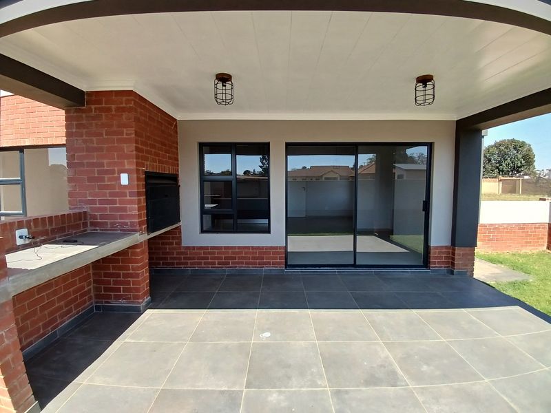 A modern covered patio featuring a built-in brick braai, concrete prep surface, tiled flooring, and large sliding glass doors leading into the home.