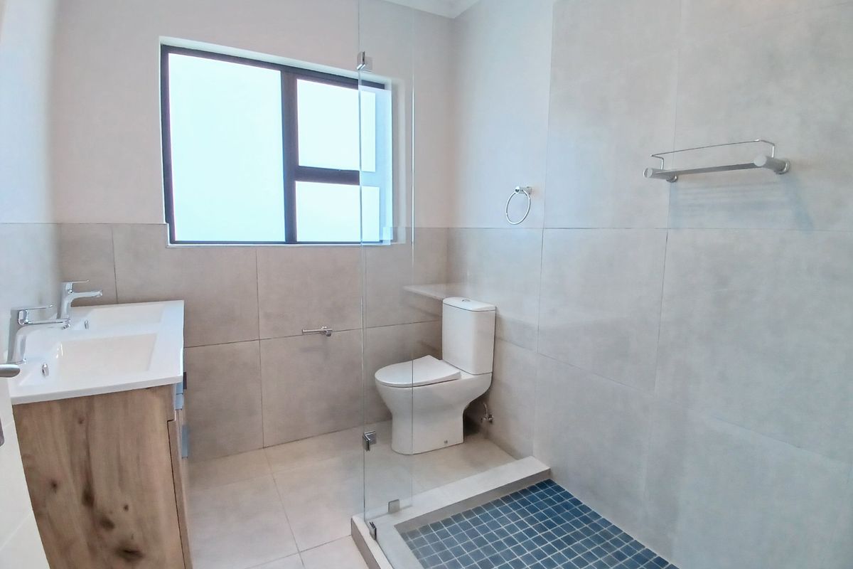 Modern bathroom featuring a double vanity, glass-enclosed shower with mosaic floor tiles, and neutral wall tiling.