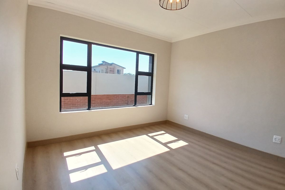 A bright, empty bedroom featuring modern laminate flooring, neutral walls, and large black aluminium windows that allow for ample natural light.