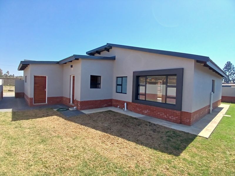 A modern single-story residential home featuring a combination of plastered walls and a brick plinth, with aluminium window frames and a neat lawn.