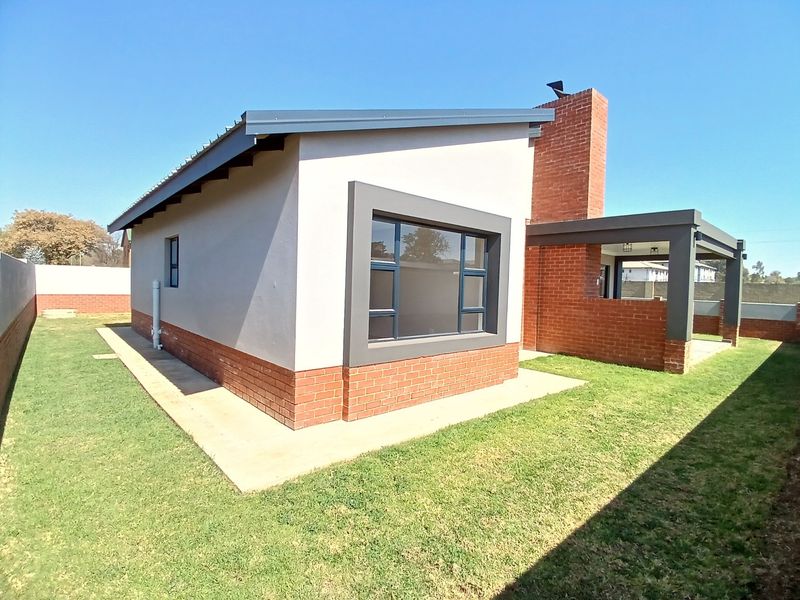 Rear view of a modern house featuring a brick chimney, covered patio area, and well-maintained lawn with concrete perimeter paving.