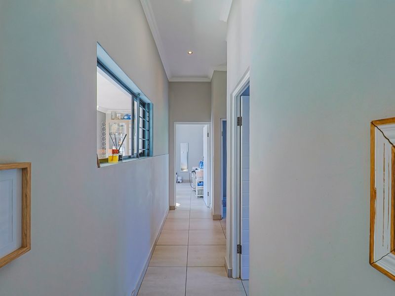 A bright and clean hallway featuring neutral tiled flooring, coving, and an internal window providing a view into the adjacent room.