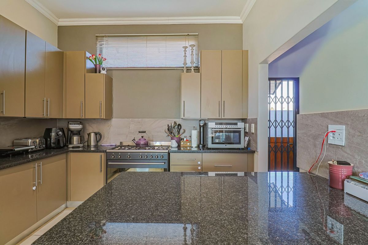 A functional kitchen featuring granite countertops, ample built-in cabinetry, a gas stove, and an oven, with direct access to an exterior security gate.