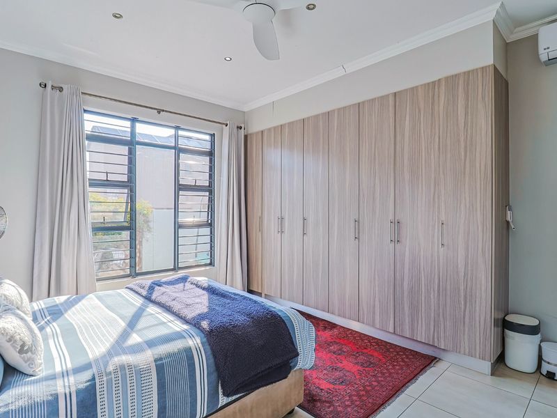 A well-maintained bedroom featuring extensive built-in cupboards, tiled flooring, a ceiling fan, and a wall-mounted air conditioning unit.