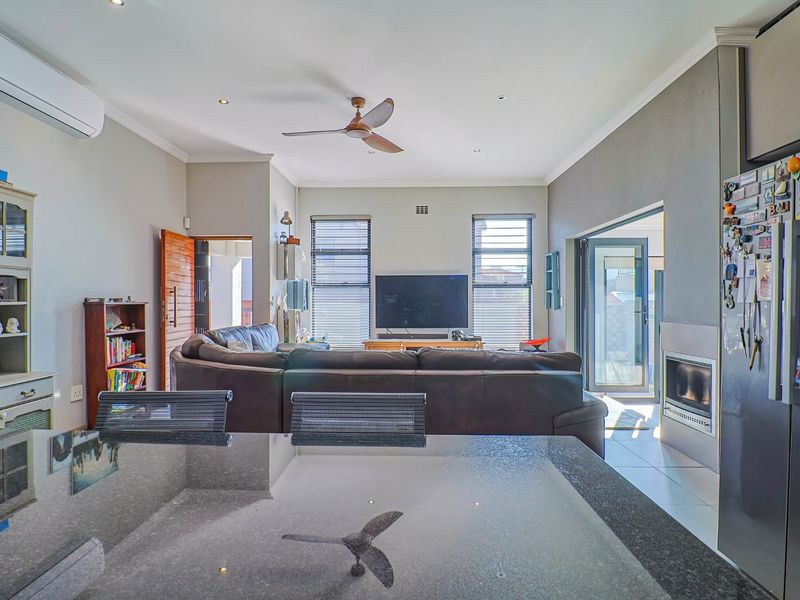 Spacious open-plan living area featuring a modern fireplace, tiled flooring, ceiling fan, and split-system air conditioning, seamlessly connecting to the kitchen and outdoor space.