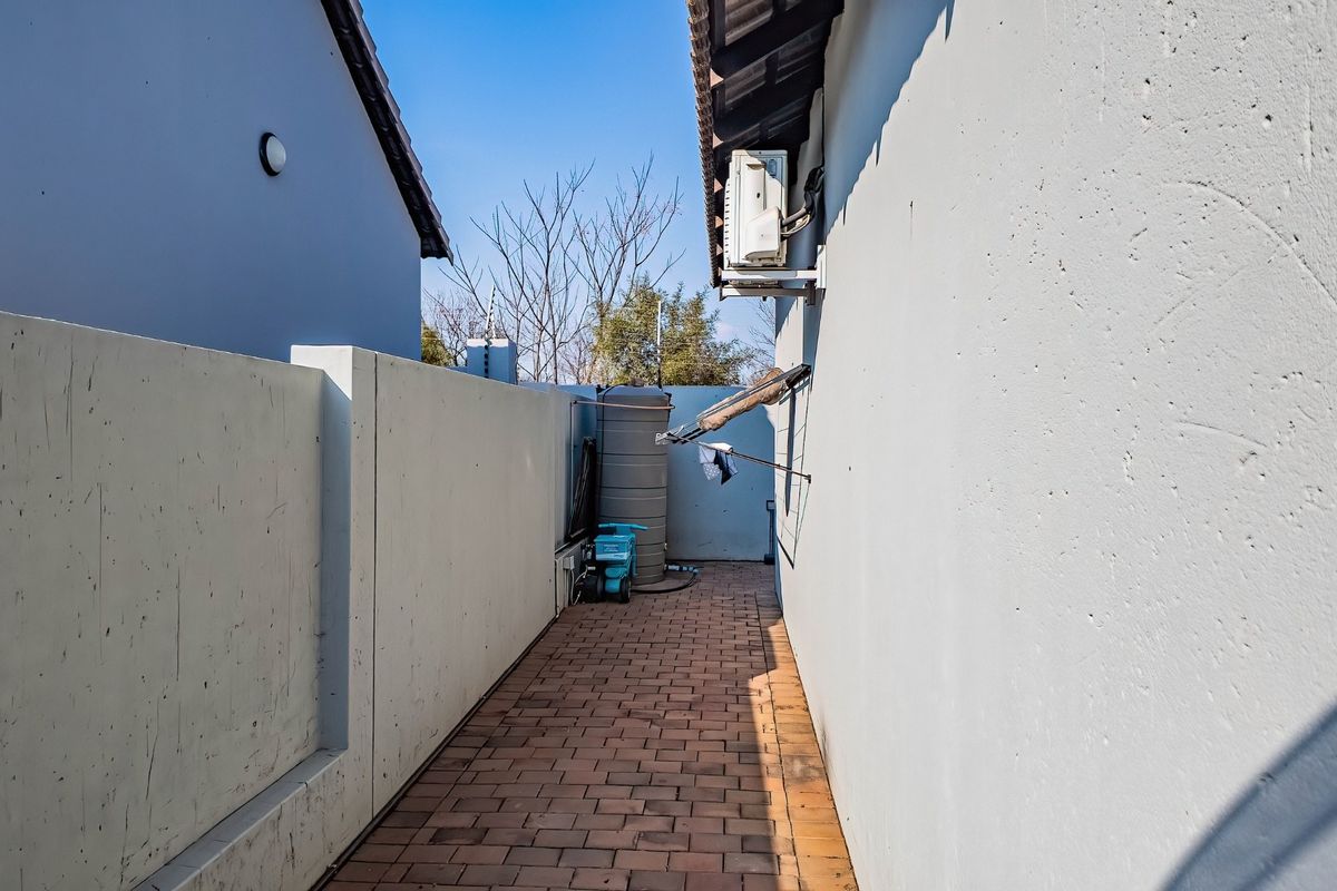 A narrow side passage featuring brick paving, a water storage tank, and an external air conditioning unit mounted on the building wall.
