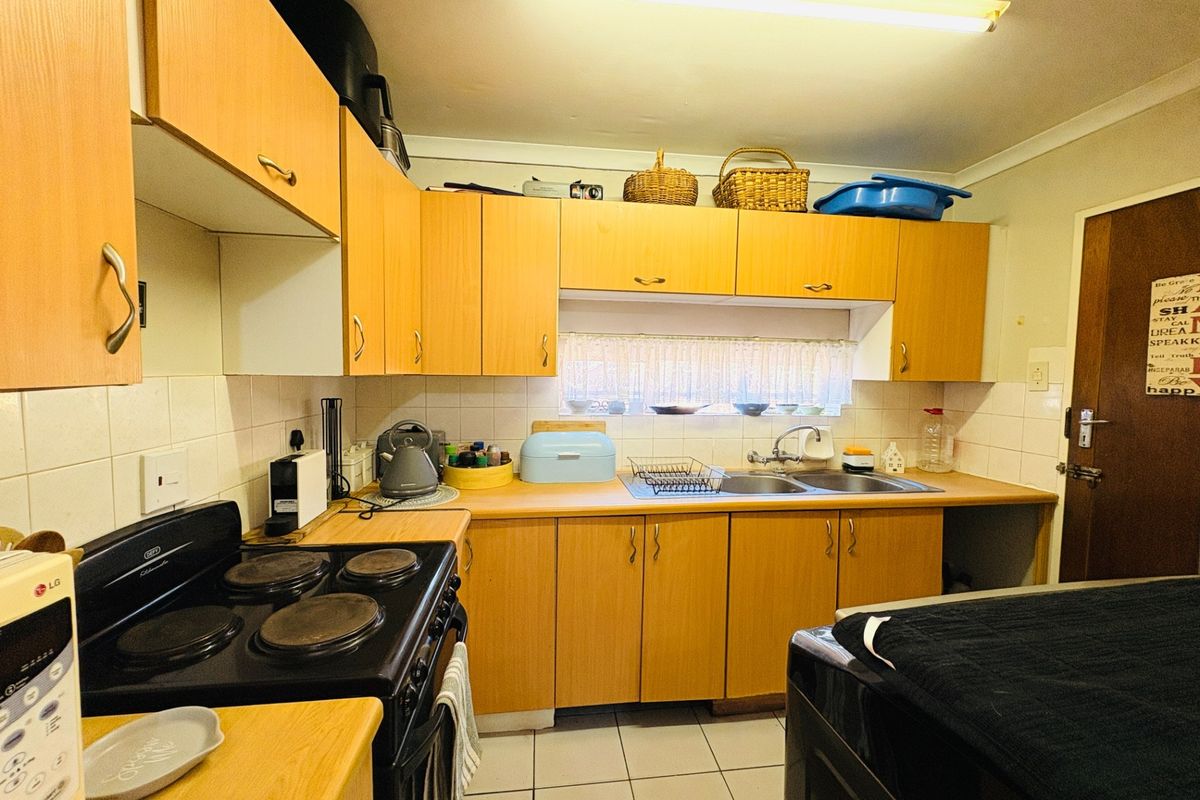 A functional kitchen featuring light wood-tone cabinetry, laminate countertops, a double stainless steel sink, and a built-in electric stove with tiled backsplash.