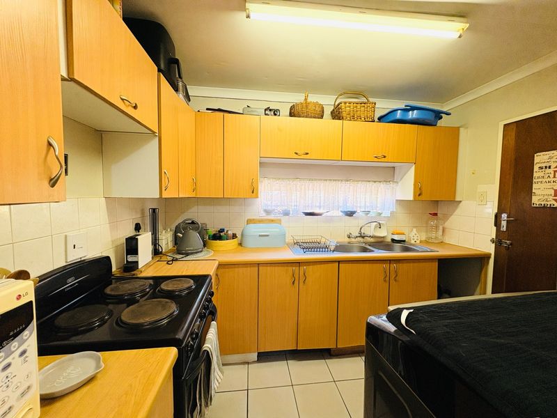 A functional kitchen featuring light wood-tone cabinetry, laminate countertops, a double stainless steel sink, and a built-in electric stove with tiled backsplash.