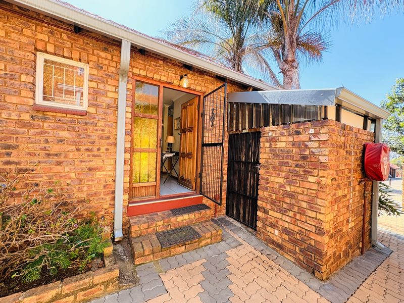 Front entrance of a face brick townhouse featuring a secure gated entry, paved walkway, and exterior brick detailing.
