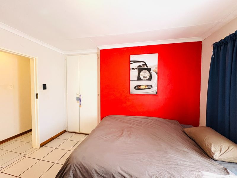 A bedroom featuring tiled flooring, built-in cupboards, and a bold red accent wall, providing a functional space with potential for modern updates.