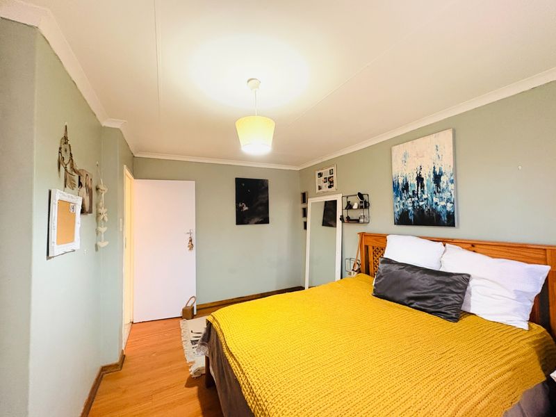 A bedroom featuring laminate flooring, coved ceilings, and a central pendant light fixture, finished with light green wall paint.