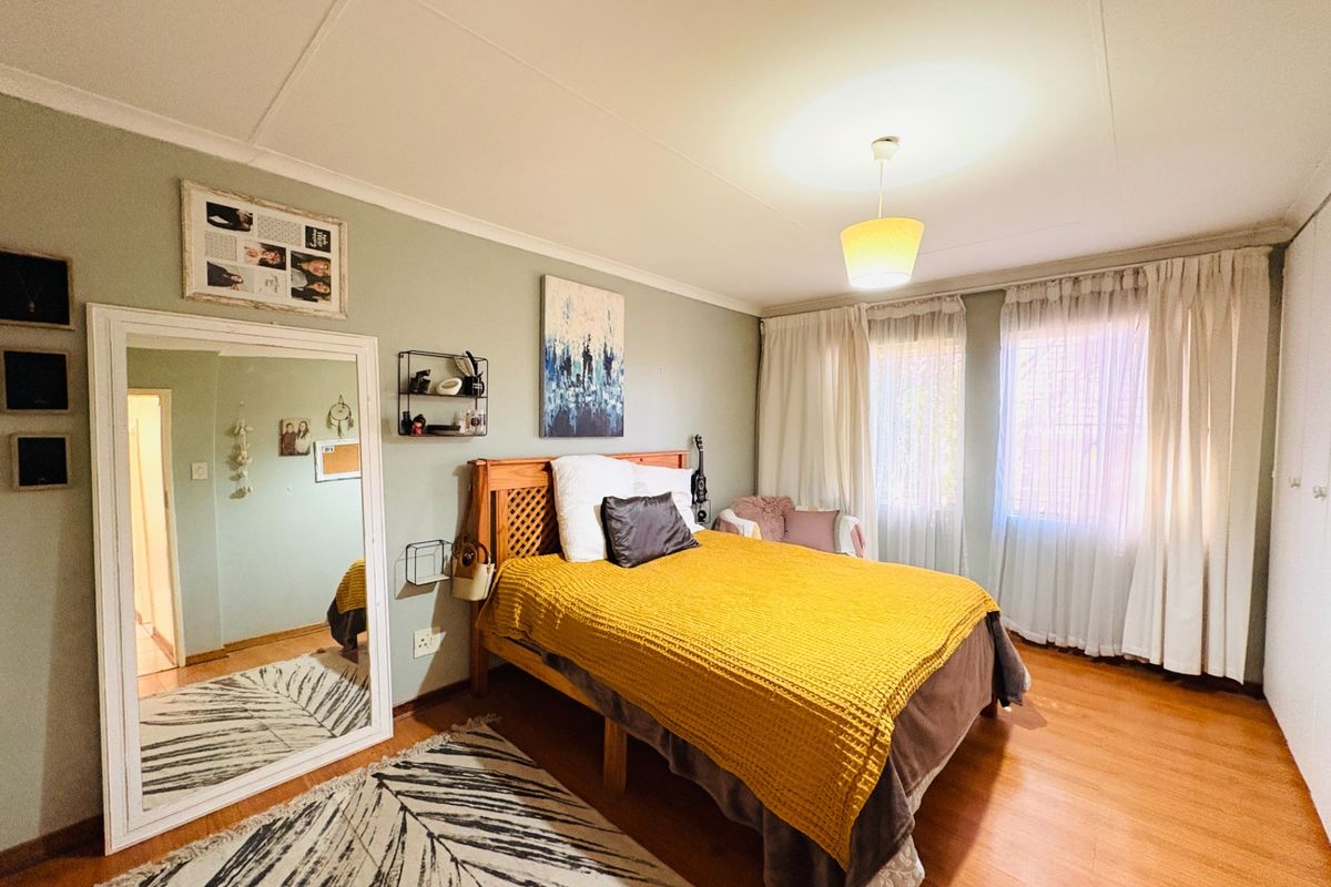 A well-lit bedroom featuring laminate flooring, neutral wall tones, and built-in wardrobe storage, offering a comfortable and functional living space.