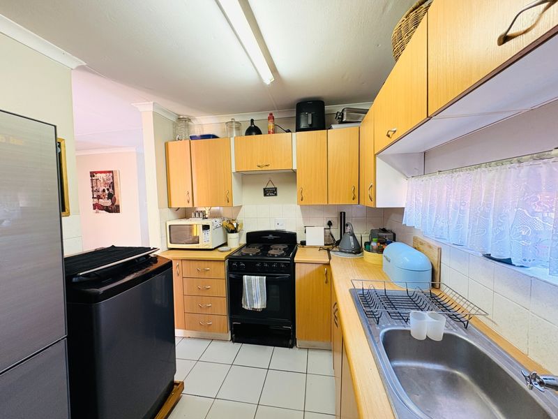 A functional kitchen featuring light wood-finish cabinetry, a tiled backsplash, tiled flooring, and a built-in electric stove with a stainless steel sink.