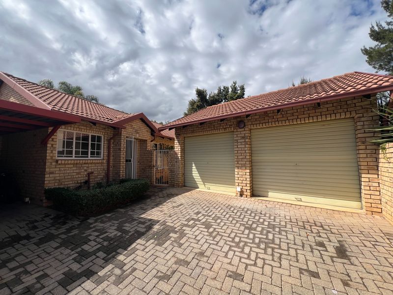 Front exterior view of a townhouse featuring a double garage with roll-up doors, face brick construction, and a paved driveway.