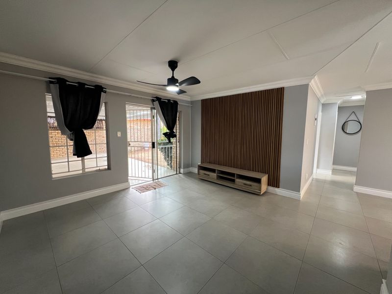 A bright living room featuring large format floor tiles, a modern slatted wood feature wall, and a ceiling fan, with direct access to the exterior.