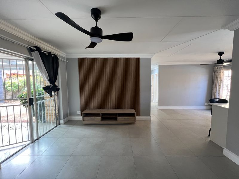 Spacious open-plan living area featuring modern slatted wood wall paneling, neutral tiled flooring, ceiling fans, and direct access to an outdoor patio area.