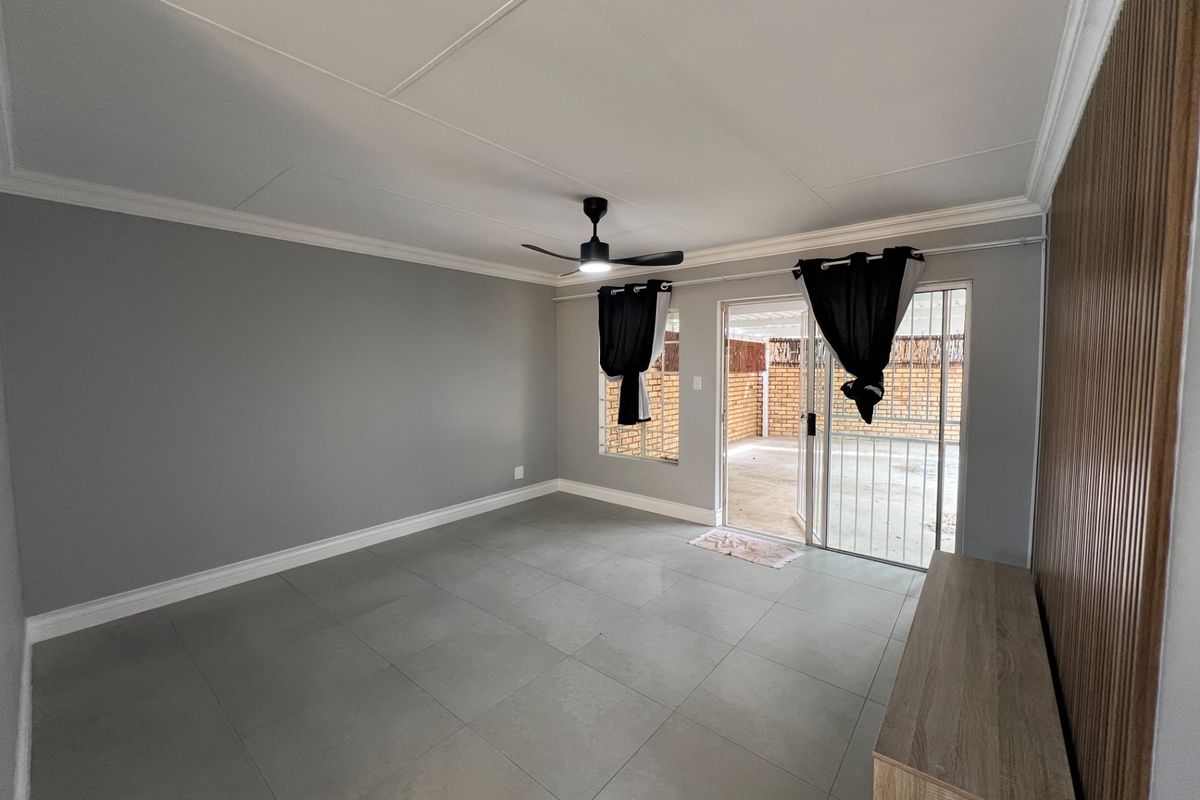 Spacious living area featuring neutral grey tiled floors, a ceiling fan, and sliding glass doors providing direct access to the outdoor patio area.