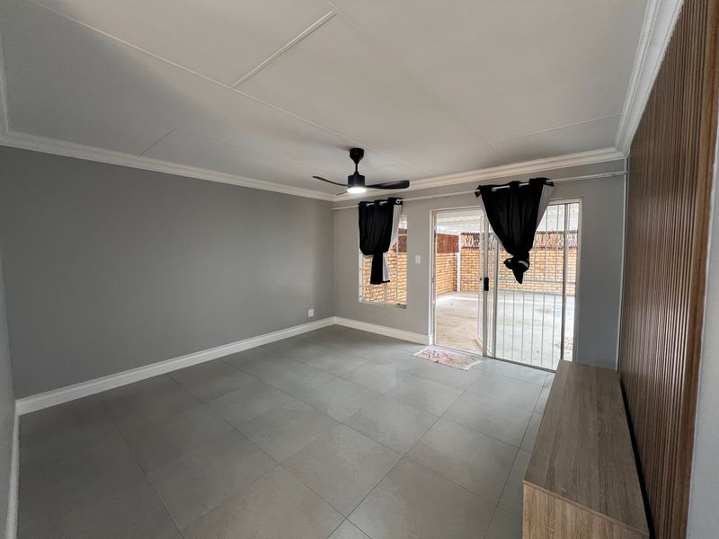 Spacious living area featuring neutral grey tiled floors, a ceiling fan, and sliding glass doors providing direct access to the outdoor patio area.