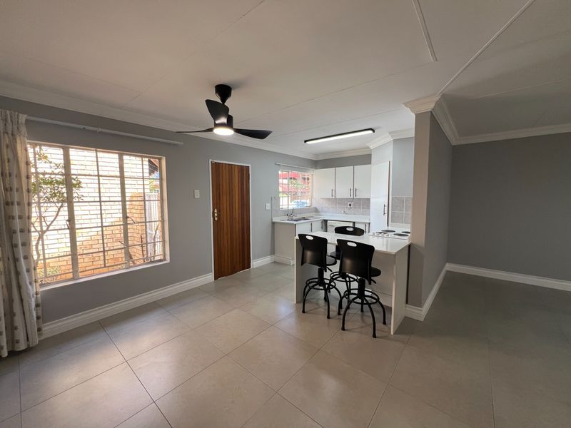 Open-plan living and kitchen area featuring tiled floors, a breakfast counter, built-in cabinetry, and a ceiling fan in a well-maintained townhouse setting.