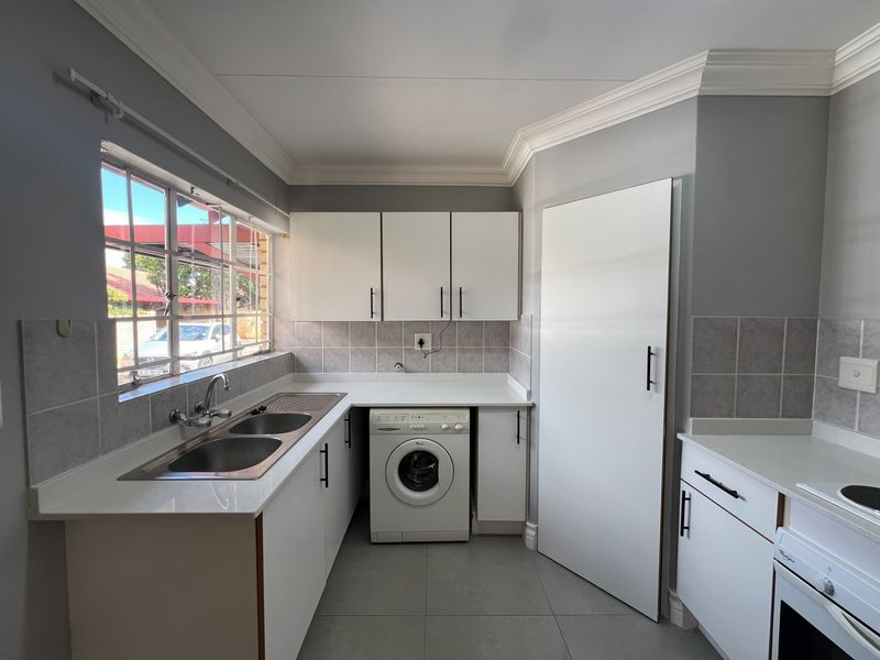 Modern kitchen featuring white cabinetry, quartz countertops, double basin sink, integrated washing machine, and built-in oven with hob.
