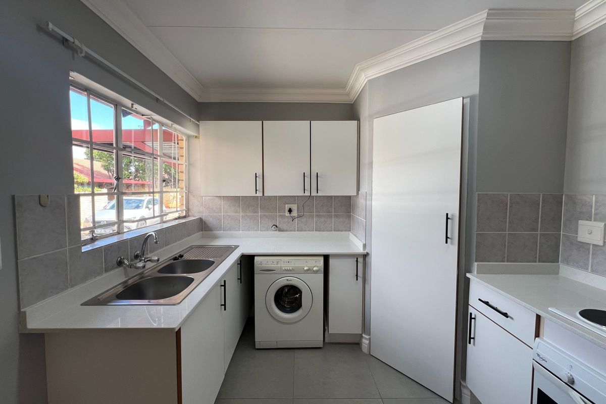 Modern kitchen featuring white cabinetry, quartz countertops, double basin sink, integrated washing machine, and built-in oven with hob.